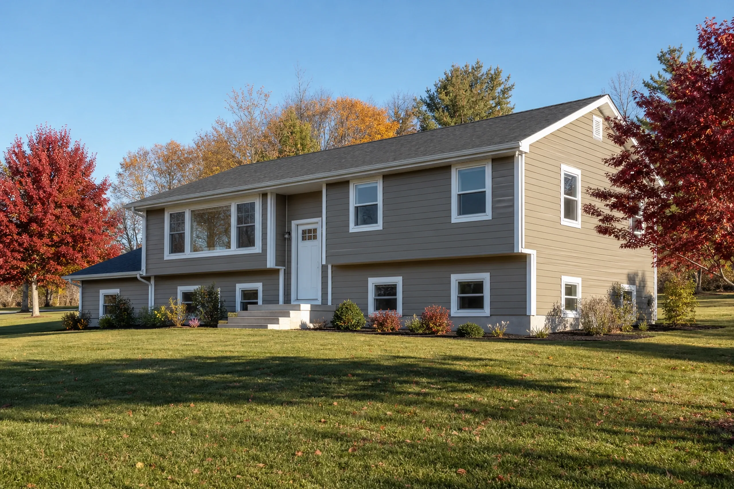 James Hardie fiber cement siding in the Lewiston-Auburn area: a 1970s raised ranch finished in smooth khaki fiber cement lap boards with crisp white trim, a mown lawn and red maples, early fall.