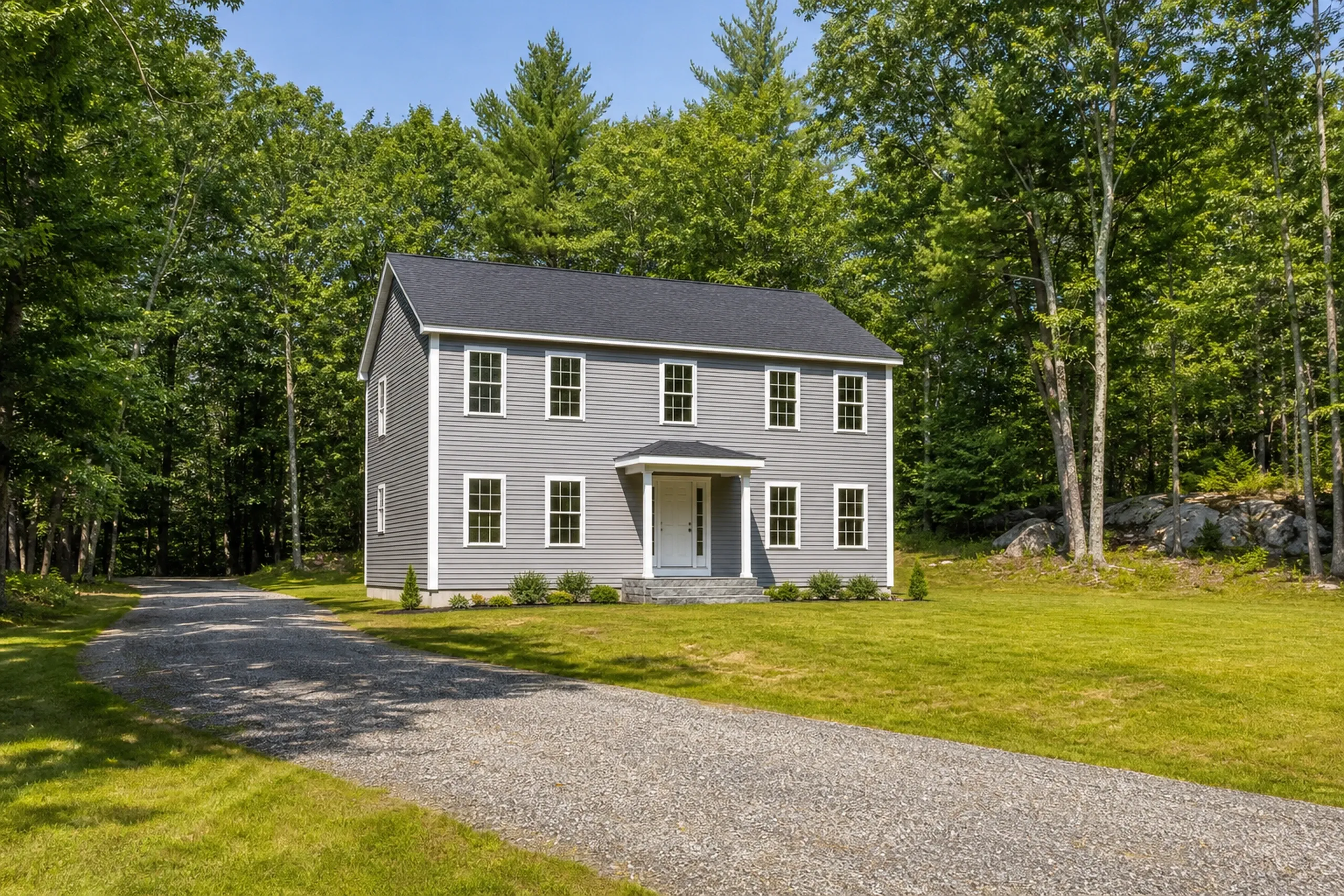 Vinyl lap siding on an Otisfield 1990s colonial: a two-story house on a wooded back-road lot in finished soft-gray vinyl lap, white corner posts and window trim, midsummer.