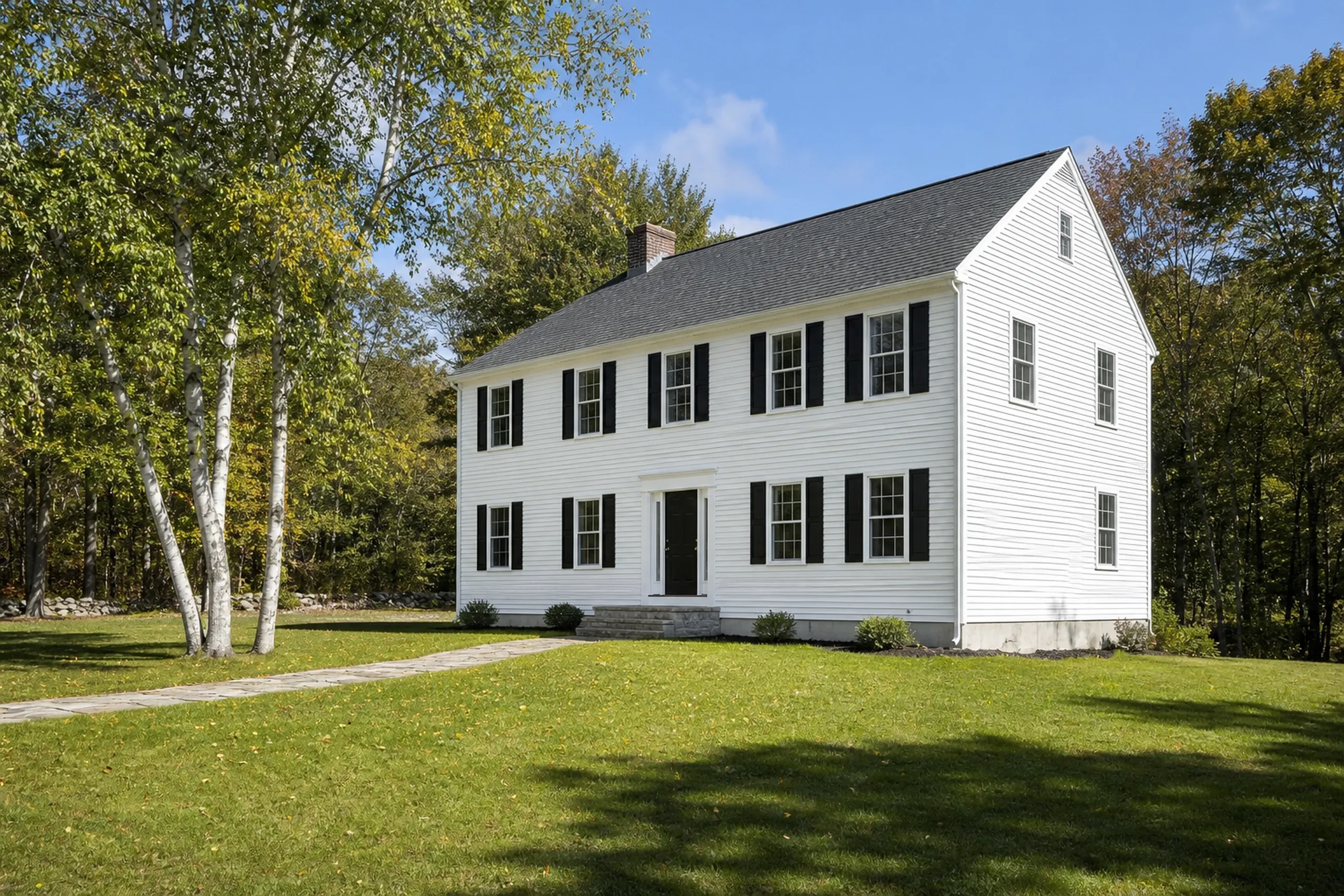 Vinyl siding on a Poland village home: a two-story 1980s colonial with finished soft white vinyl lap siding, black shutters and white trim, a lawn and birches, early fall.